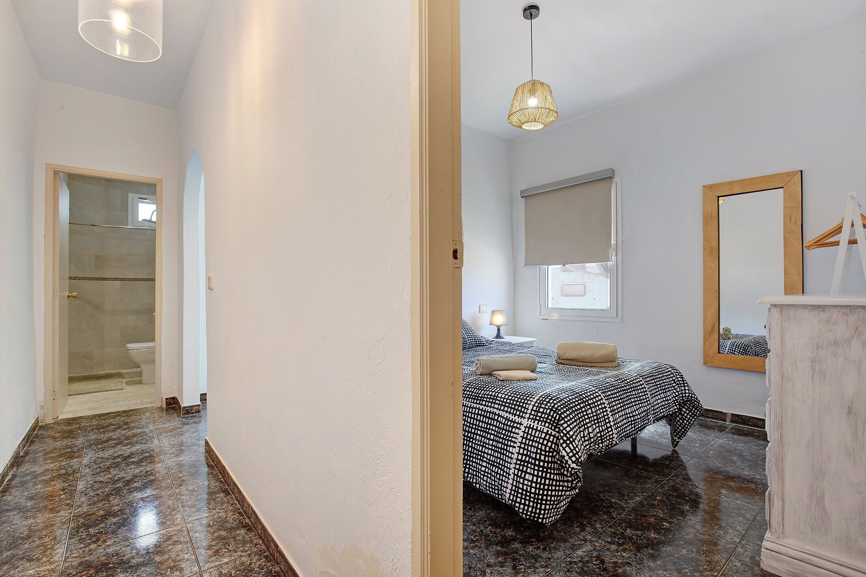 Een slaapkamer met een bed, nachtkastje, lamp en een spiegel aan de muur.
