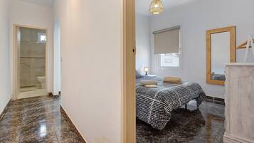 Een slaapkamer met een bed, nachtkastje, lamp en een spiegel aan de muur.