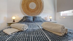 Een slaapkamer met een bed met een decoratief sprei, twee bedlampen, een grote ronde wanddecoratie en een raam met een zonwering.