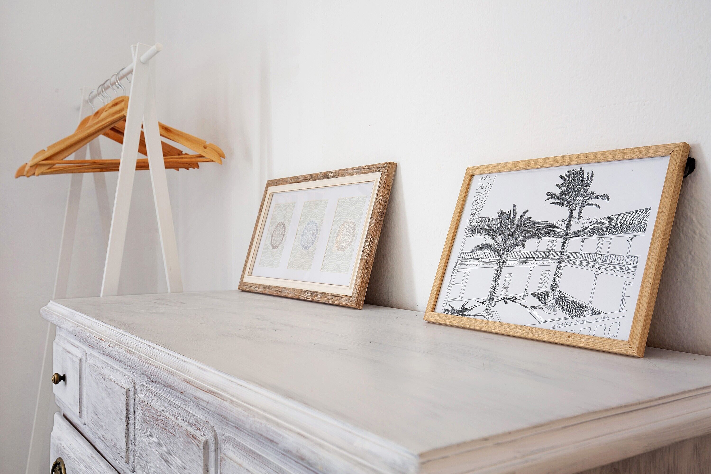 A white dresser with two framed pictures, one with a geometric design and the other depicting a building with palm trees.