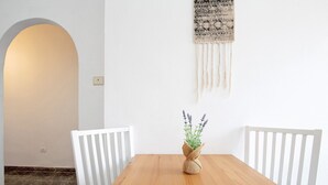 Een houten eettafel met witte stoelen, een geweven plantenhouder en een wanddecoratie van macramé.