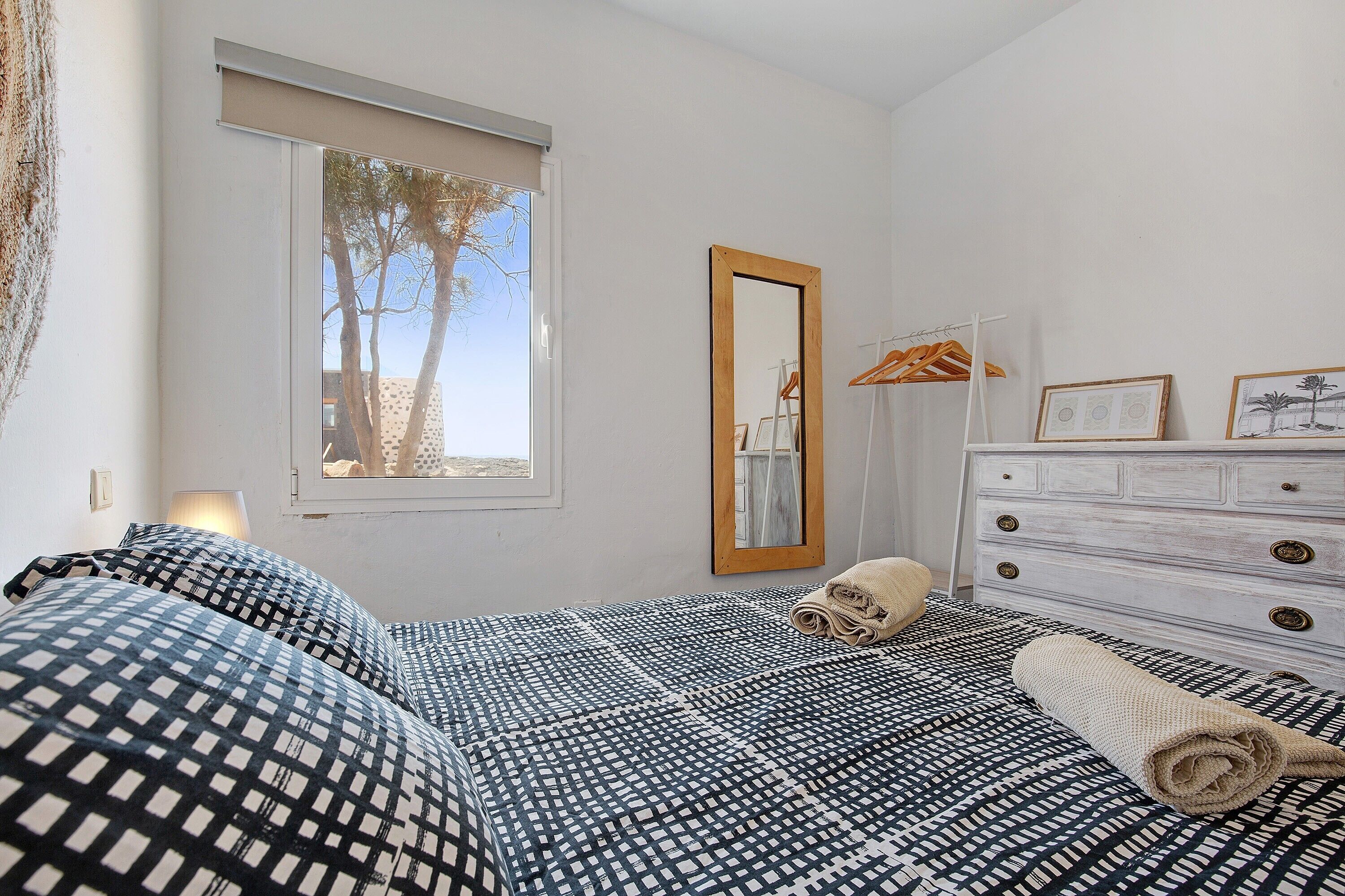 Una camera da letto con un letto, una cassettiera, uno specchio e una finestra vista alberi.