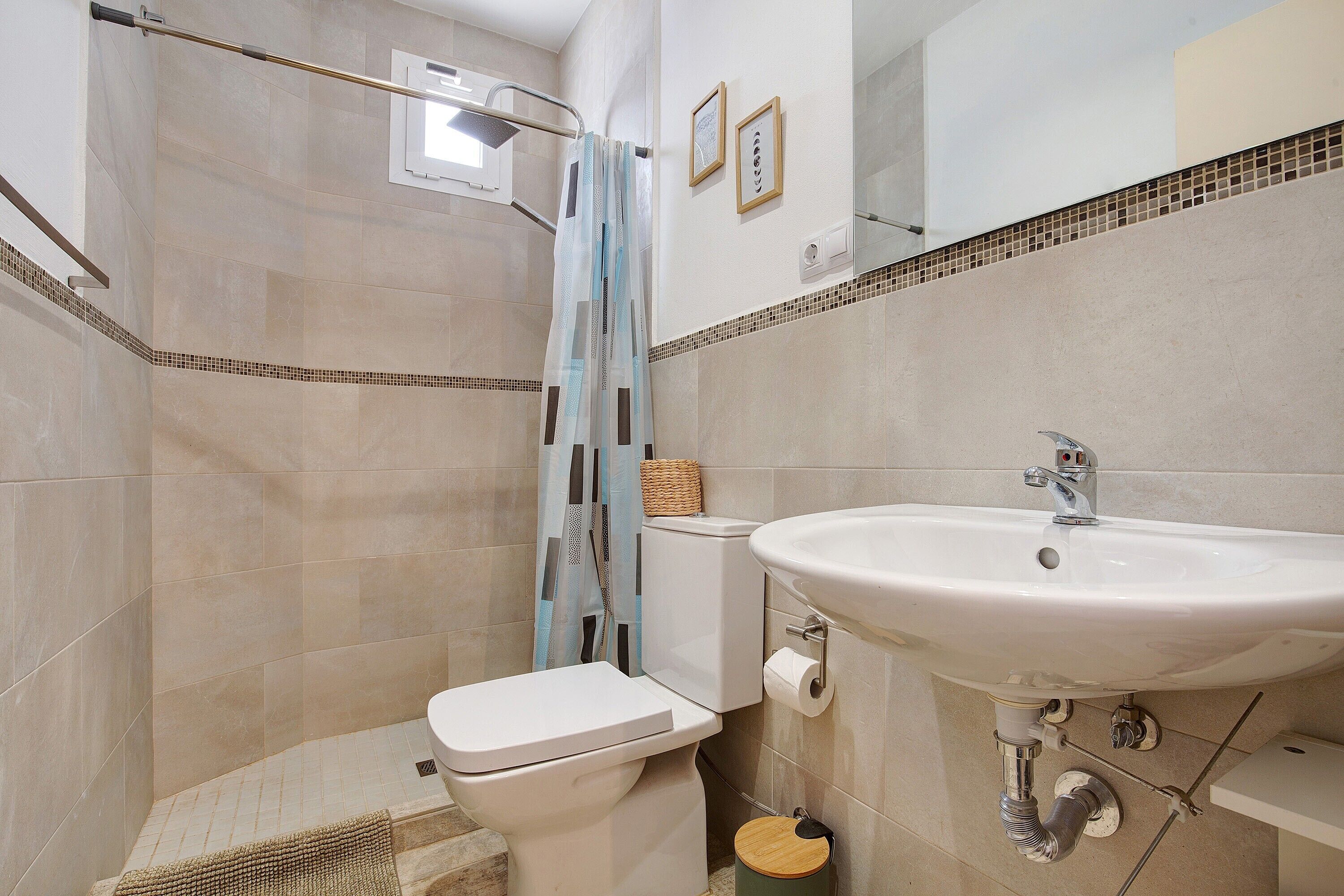 A bathroom with a toilet, shower, sink, and tiled walls.