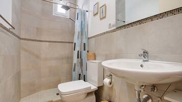 A bathroom with a toilet, shower, sink, and tiled walls.