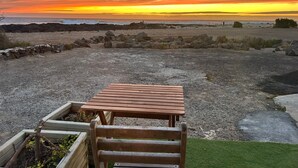 Een houten bank en tafel in een tuin met uitzicht op zee en de ondergaande zon.