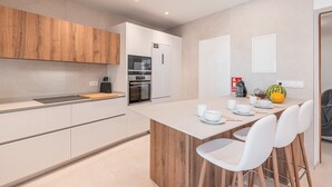 A modern kitchen with a central island, white cabinetry, and a wooden accent wall. - Holiday Home Casa en Sineu with Mountain View, Terrace & Wi-Fi (Sineu)