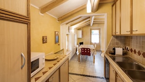 A kitchen with wooden cabinets, a microwave, a sink, and a dining area with a table and chairs. - Appartamento Giada with Mountain View, Balconies & Wi-Fi (Livigno)