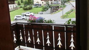 A wooden balcony with a view of a mountain, a building with balconies, and parked cars. - Appartamento Giada with Mountain View, Balconies & Wi-Fi (Livigno)