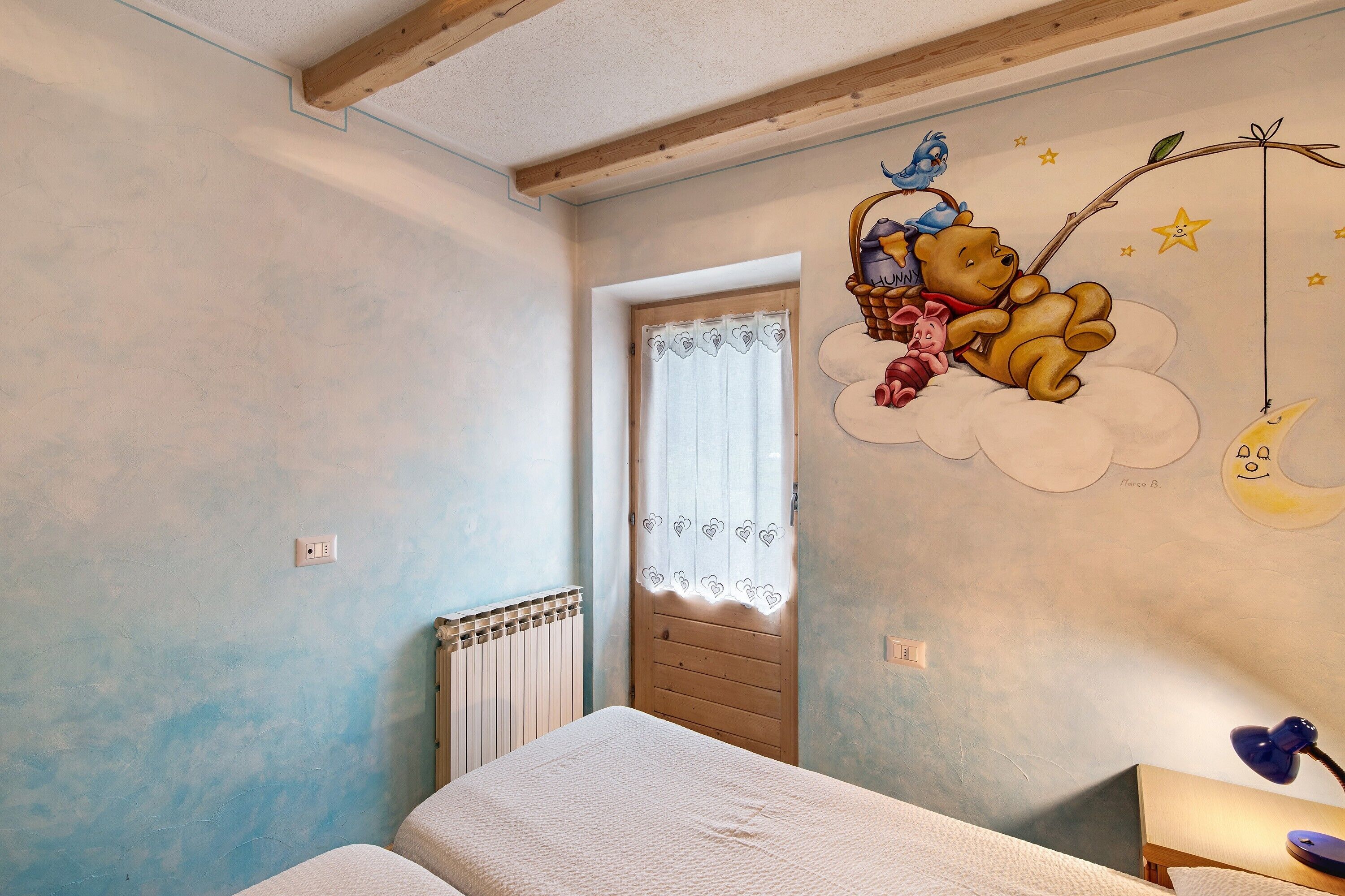 A child's bedroom with a bed, a nightstand, a window with curtains, and a wall mural.