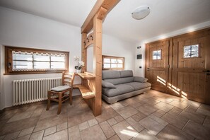A room with a wooden desk, a grey sofa, a radiator, and wooden doors.
