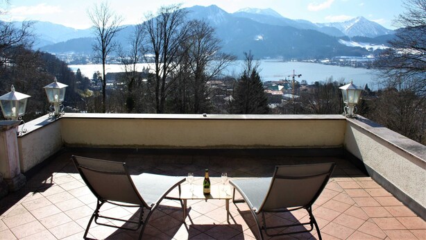 A terrace with two chairs and a table, overlooking a lake and mountains. - Vacation apartment SeeFugium (Tegernsee)