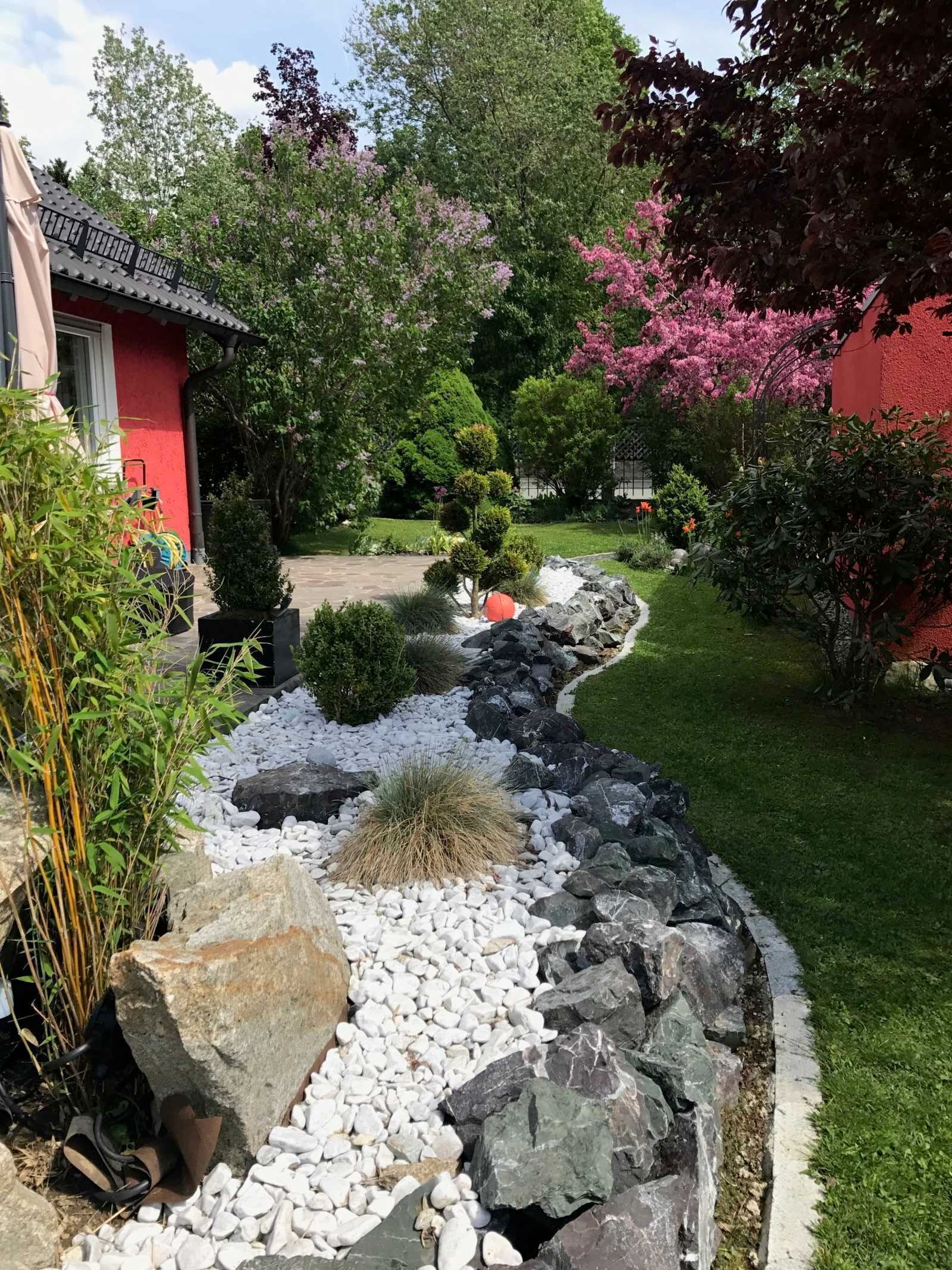 Un jardin avec un sentier, des rochers et différentes sortes de plantes.