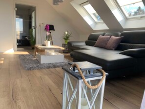 A modern living room with a black sofa, a white coffee table, and a glass-top table with a rope handle.