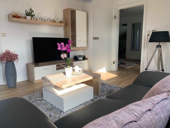 Una sala de estar moderna con un televisor de pantalla plana, una mesa de centro con objetos decorativos, un sofá y una lámpara.