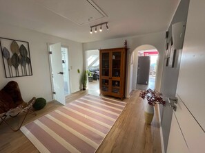 A spacious room with a wooden floor, a striped rug, a cabinet with glass doors, and a plant.