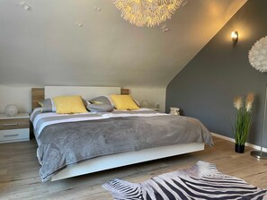Un dormitorio moderno con techo inclinado, una cama grande con ropa de cama estampada, una lámpara de pared decorativa y una alfombra con estampado de cebra.
