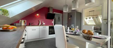 Una cocina moderna con comedor, una silla blanca, una mesa dispuesta para el desayuno y un amplio ventanal.