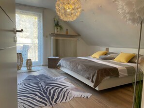 A bedroom with a bed, a radiator, a hanging light fixture, and a window with a view.