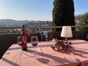 A table with a bottle and two glasses of red wine, a decorative rock, and a lamp on a balcony overlooking a landscape.