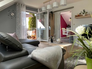 A modern living room with a sofa, a coffee table, and a view through a glass door to an outdoor area.