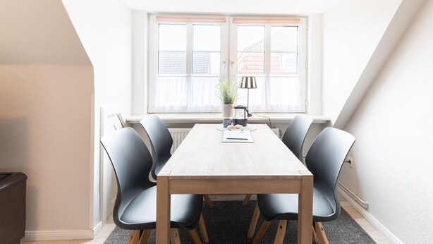 A conference room with a wooden table, six chairs, a potted plant, and a lamp.