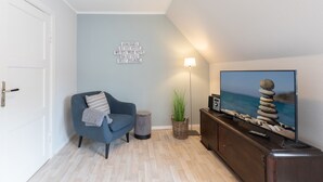 A modern living room with a blue sofa, a flat-screen TV, a wall-mounted lamp, and a decorative wall piece.