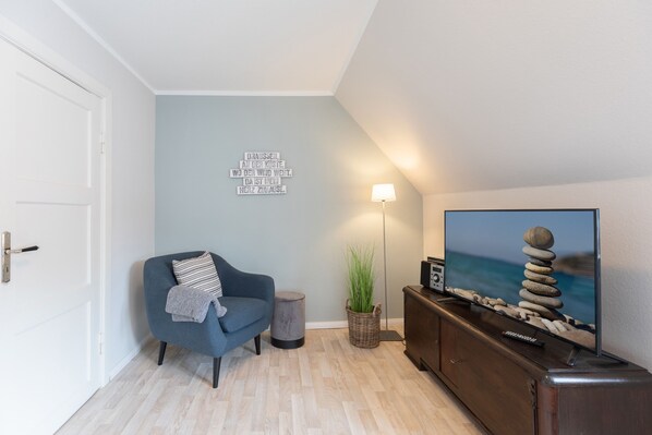 Un salon moderne avec un canapé bleu, un téléviseur à écran plat, une lampe fixée au mur et un élément décoratif mural.
