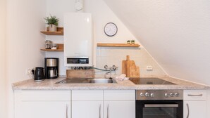 A modern kitchen with white cabinets, a stainless steel coffee maker, a built-in oven, and a clock on the wall.