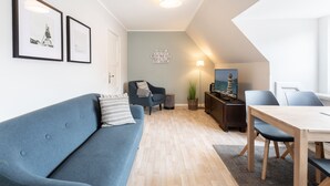 A modern living room with a blue sofa, a dining table with chairs, a lamp, and framed pictures on the wall.