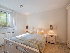 Un dormitorio con cama, mesitas de noche, cómoda y ventana con cortinas.