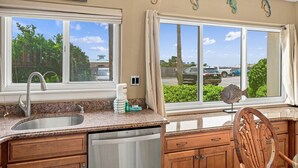 A kitchen with a double sink, wooden cabinets, and a view of a parking lot through large windows.
