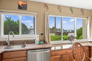 A kitchen with a double sink, wooden cabinets, and a view of a parking lot through large windows.