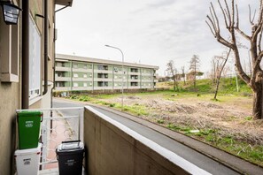 A balcony with two trash bins, a street, and a multi-story building in the background.