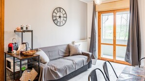 Ein modernes Wohnzimmer mit einer Couch, einer Kaffeestation, einer Uhr und einem großen Fenster.