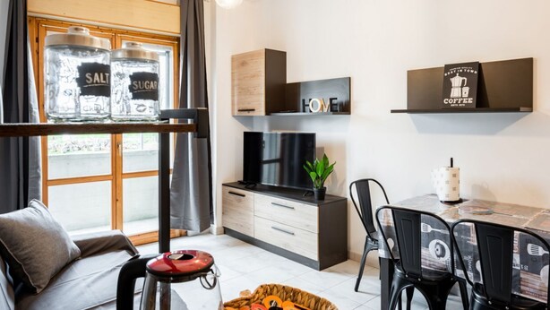 Ein modernes Wohnzimmer mit einer Couch, einem Esstisch mit Stühlen, einem Fernseher und Wanddekoration.