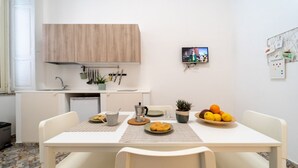 Cocina compacta con un mueble de madera, un televisor pequeño y una zona de comedor con una mesa para dos.