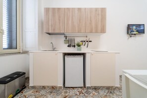 Una cocina compacta con armarios de madera, un refrigerador pequeño y una ventana con persianas.