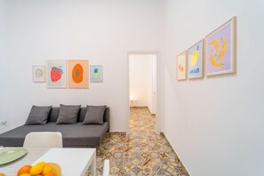Una habitación pequeña y moderna con un sofá, una mesa con fruta y obras de arte enmarcadas en las paredes.