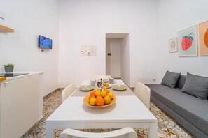 Un comedor con una mesa preparada para dos personas, un frutero y un televisor en la pared.