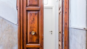Una puerta de madera con un tirador de latón, una puerta blanca al fondo y una pared con textura.