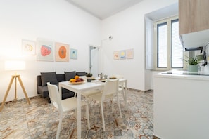 Une cuisine moderne avec des meubles blancs, une table à manger avec des chaises et une fenêtre avec des stores.