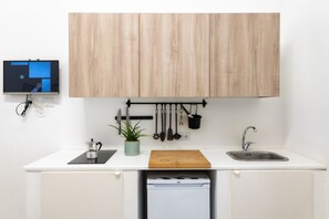 A kitchen with a wooden cabinet, a sink, a countertop, a coffee maker, a plant, and hanging utensils. - Cozy flat of 40 sqm, for 3 people, located on the raised ground floor of a renovated period building (some steps at the entrance). The property is located a few steps from the Syracusan Forum and just 200mts from the Santa Lucia Bridge which leads to the (Siracusa)