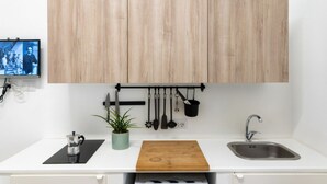 Een keuken met een wit aanrecht, houten kastjes, een hangende pannendroger, een spoelbak en een koffiezetapparaat.