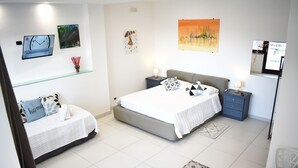Ein modernes Schlafzimmer mit einem großen Bett, einer kleinen Sitzecke, einem Nachttisch und einer Wanduhr.