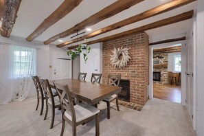 Un comedor con chimenea de ladrillo, vigas de madera y una mesa redonda con sillas.
