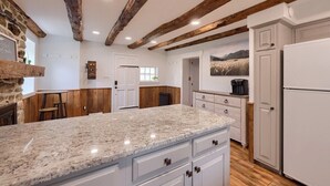 A kitchen with granite countertops, wooden beams, white cabinetry, and a stone fireplace. - Peaceful Hollow - Peaceful Hollow (Manchester)