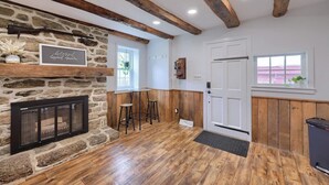 A room with a stone fireplace, wooden beams, a white door, and a window with a view. - Peaceful Hollow - Peaceful Hollow (Manchester)