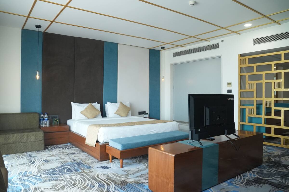 A hotel room with a bed, a TV, a bench, a sofa, and a patterned carpet.