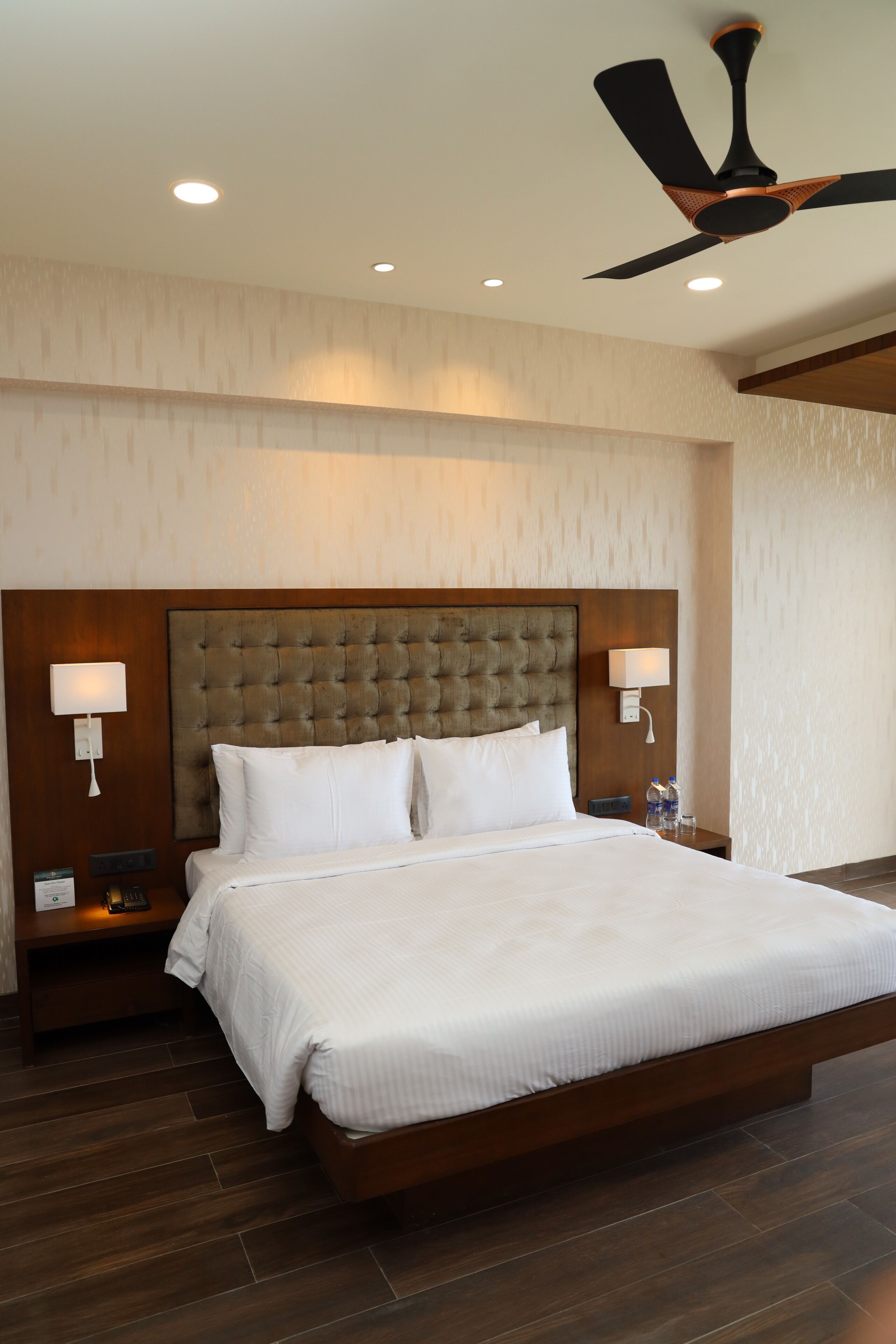 A hotel room with a large bed, a ceiling fan, recessed lighting, and a wooden headboard.
