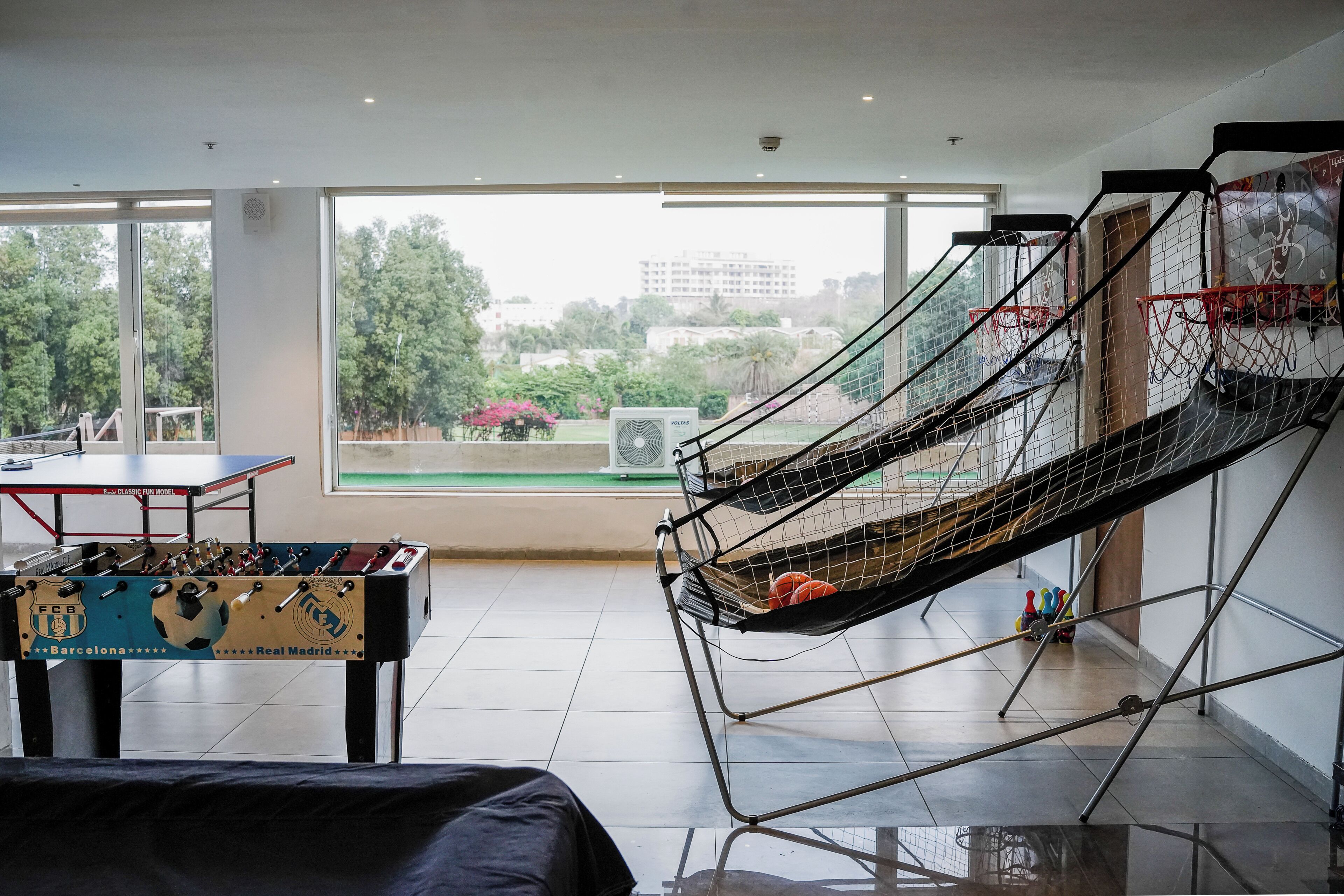 A room with a foosball table, a hammock, and a view of trees and buildings outside.